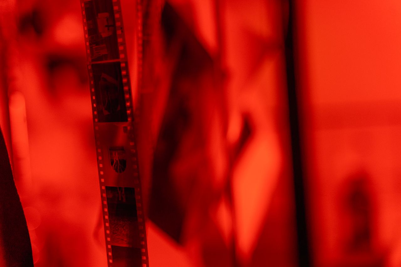 faq-img Close-up view of film negatives hanging in a darkroom under red lighting.